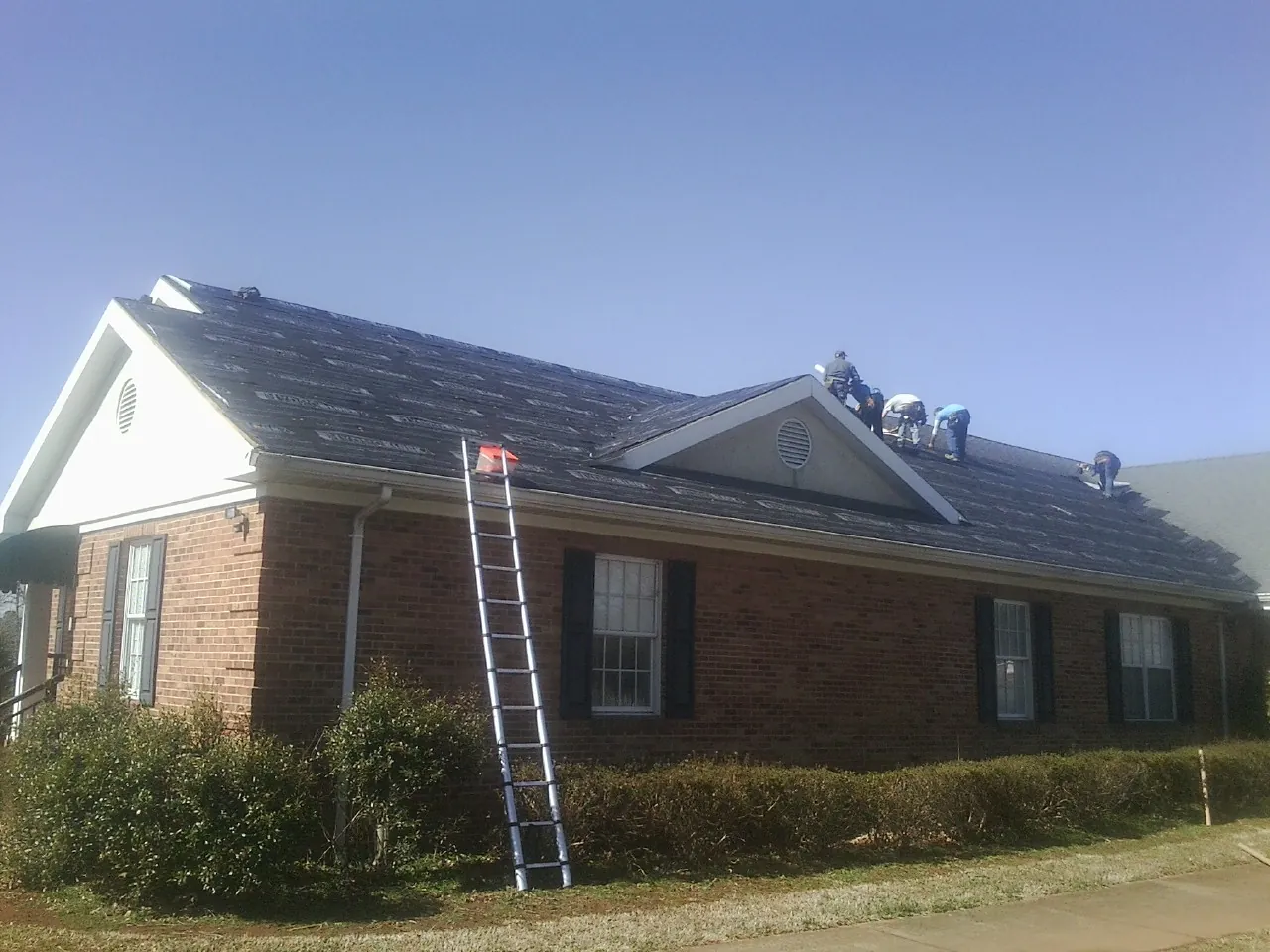 Crew tearing shingles off a brick ranch roof with a ladder set — Metal Roof Repair work by our crew in Bretton Woods