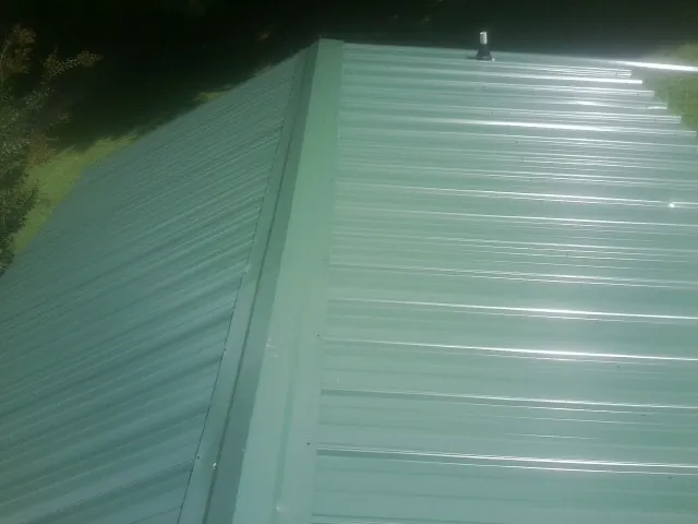 New green metal panels meeting at the ridge of a roof — Flat Roof Repair work by our crew in Bretton Woods