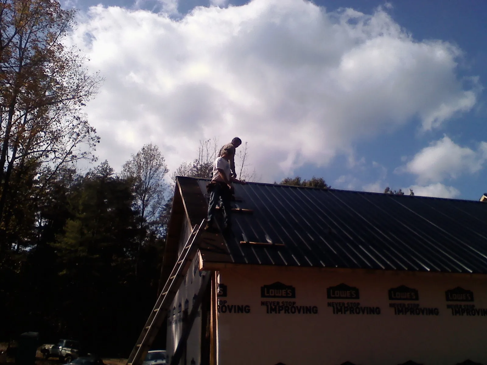 Roofer fastening dark metal panels high against a cloudy sky, from a Roof Inspection job in Bretton Woods