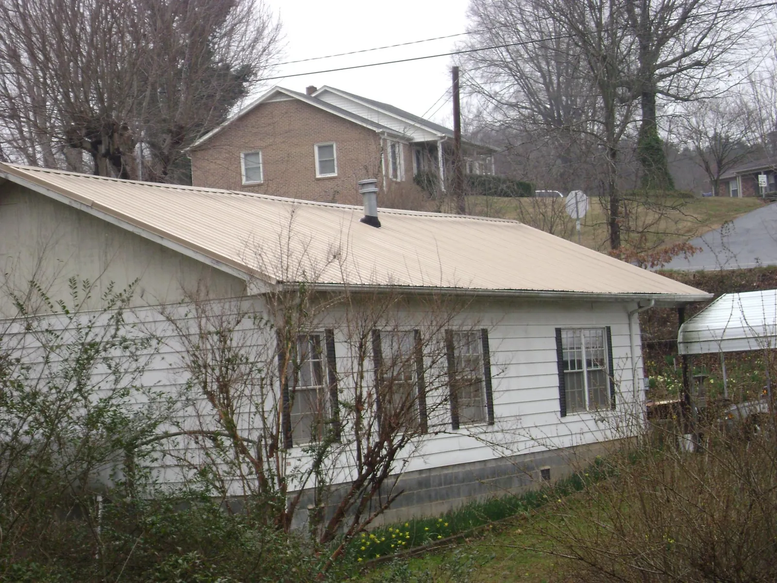 Tan metal roof on a white sided house set into a hillside — Commercial Roofing by Roofing Brothers in Bretton Woods