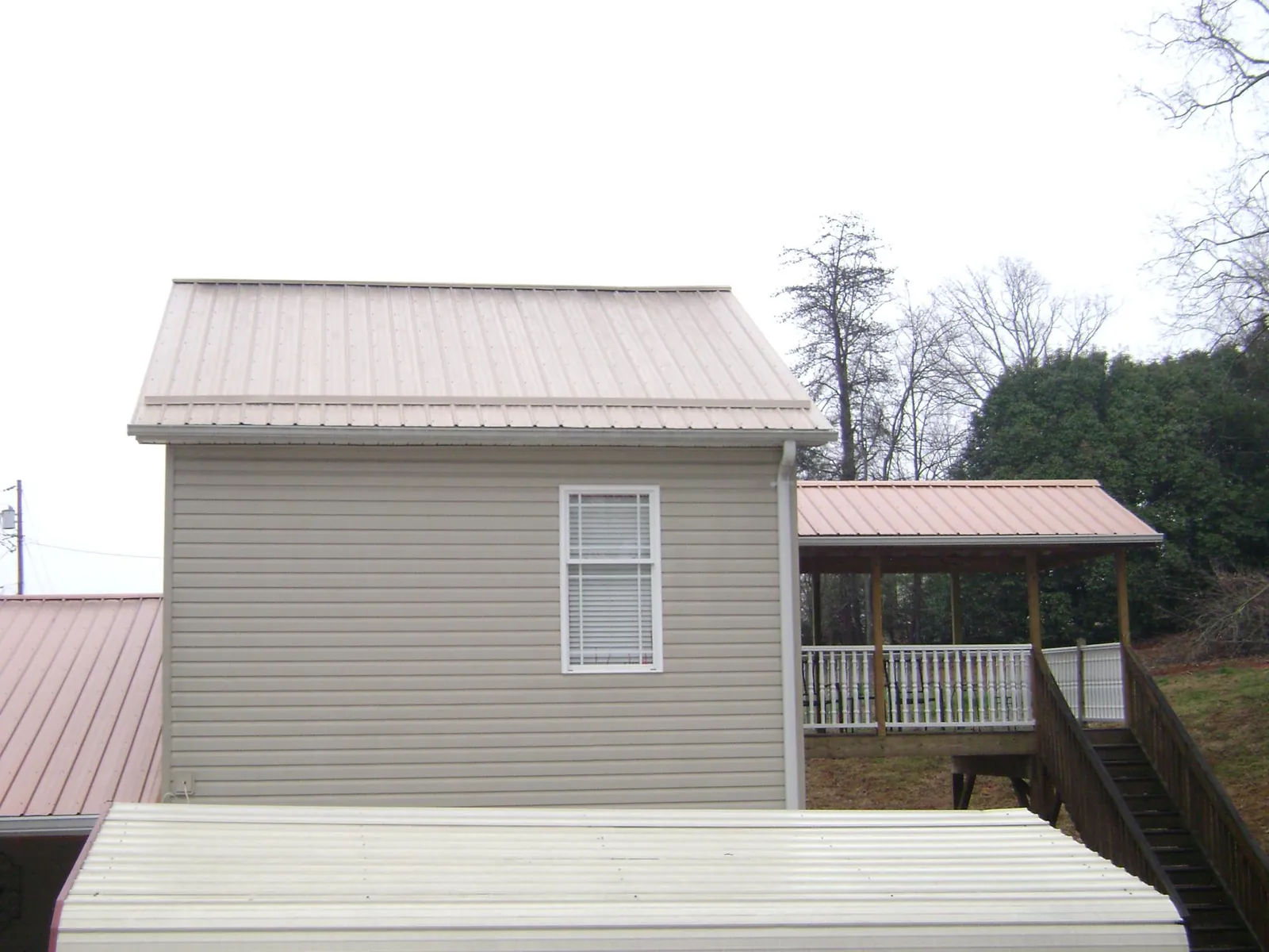 Tan metal roofs on a two story addition and attached porch, from a Roof Replacement job in Bretton Woods
